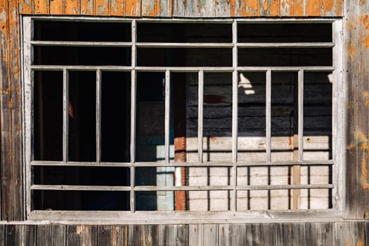 Sunlight illuminating old broken window with bars and peeling paint on wooden wall in abandoned house