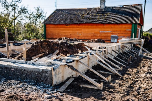 Construction workers building strip foundation for new house near old wooden house