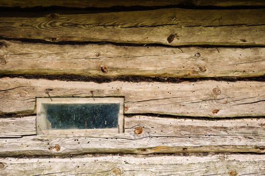 Old weathered wooden wall with small dirty window of abandoned house in countryside