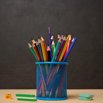 Multi-colored pencils in a blue metal cup, sharpener and erasers symbolizing study or creativity