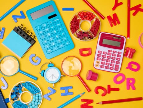Colorful school supplies, learning items calculators, letters, tools, and stationery scattered on a vibrant yellow background. Education and back to school concept