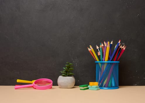 Multicolored pencils in a blue glass, a pink magnifying glass, erasers and a small plant symbolizing study or creativity are arranged on a black background with space for text