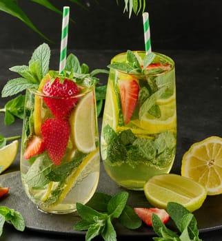 A refreshing drink in a glass with lemon slices, strawberries, fresh mint leaves, and sparkling water, served with lime and mint on a black plate