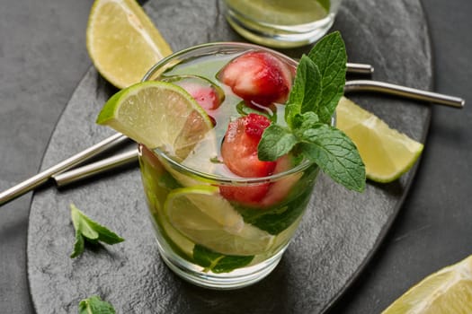 Refreshing mojito cocktail with lime, mint, strawberry, and ice on dark background, top view
