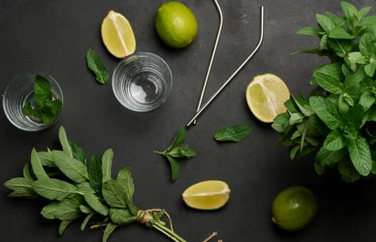 Bunch of fresh green mint on wooden table and lime wedges, glasses and metal straws, top view. Cocktail ingredient