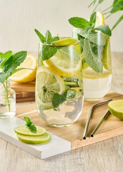Refreshing citrus and mint drink in glasses with ice, lemon, lime, and mint leaves. Healthy summer beverage
