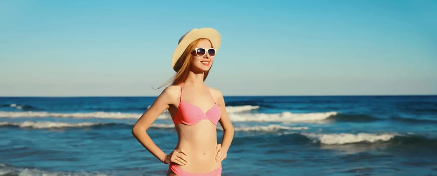 Summer vacation, beautiful happy slim woman in bikini swimsuit, tourist hat looking away standing on the beach on sunny sea coast background with waves