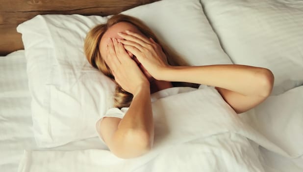 Upset sad crying woman covering her eyes and face with her hands while experiencing depression, stress, fatigue, mental suffering lying on the bed in bedroom at home