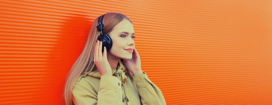 Summer portrait of happy modern young woman listening to music with headphones on orange wall background
