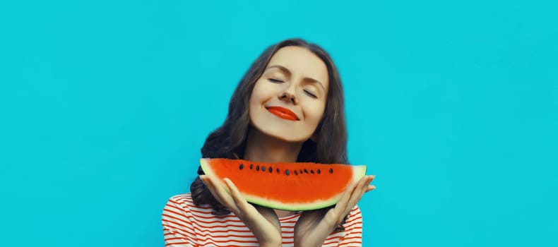 Summer portrait of happy young woman enjoying eating fresh slice of watermelon fruit on blue studio background
