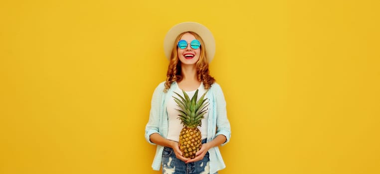 Summer vacation, happy joyful young woman with pineapple fruit in tourist hat, cheerful girl posing on yellow studio background