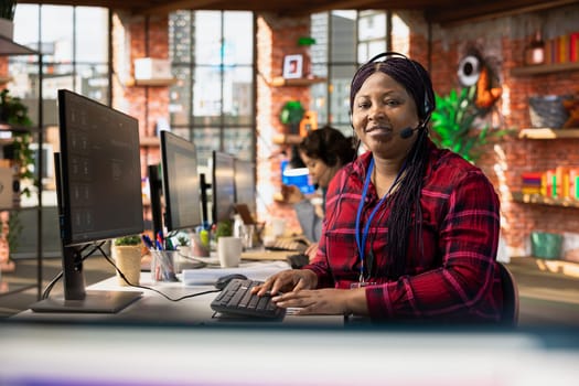 Portrait of smiling call center agent dealing with unhappy customers, speaking with them using headset at office desk. Happy woman doing customer support job, handling clients complaints in workspace