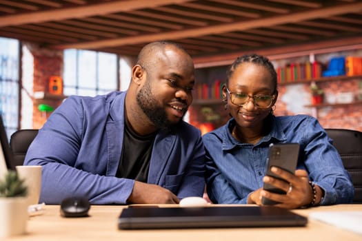 Young couple checking their email inbox before starting daily freelance work, enjoying remote tasks and scrolling through their smartphones. African american fully connected freelancers.