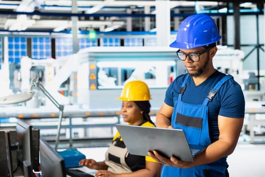 African american expert troubleshooting photovoltaic systems in solar power plant, working on a PC software for designs. Technician examines configurations in renewable energy operations.