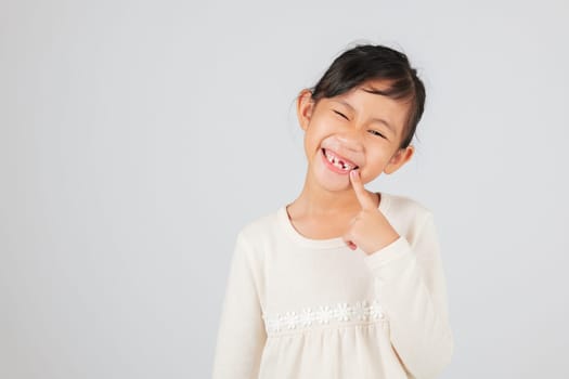 A happy child showcases a tooth gap by pointing at it. The dentist helps kids understand the stages of tooth loss and how to care for their growing tooth gap.