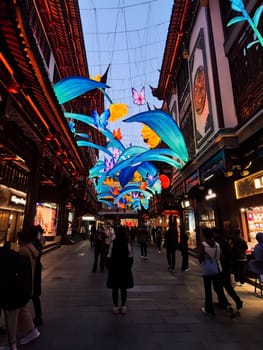 Shanghai, China - 1 April 2025: Colorful illuminated decorations with flowers and butterflies above Yuyuan Old Street in Shanghai during evening walk