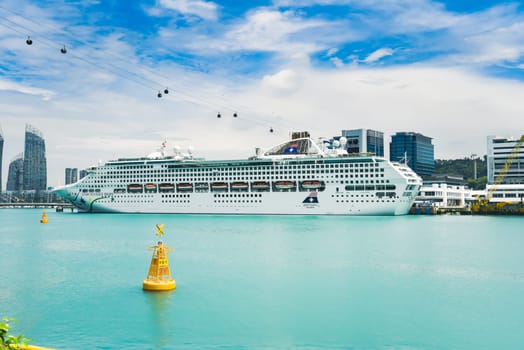 Singapore, Singapore - 4 April 2025: Star Voyager cruise ship docked at Sentosa Island terminal with cable cars above and city skyline in the background.