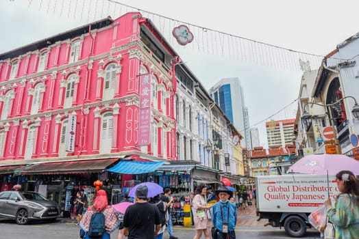 Singapore, Singapore - 4 April 2025: Colorful colonial buildings and street life in Little India. People walking with umbrellas on a rainy day in a vibrant urban scene.
