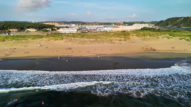 Experience a breathtaking view of surfers riding waves on a stunning beach with golden sands in a picturesque setting