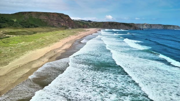 A stunning aerial view showcases a tranquil beach where gentle waves kiss the shore and reveal beautiful green cliffs
