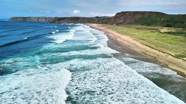 Explore this stunning aerial view of a beautiful coastline with waves crashing onto the sandy beach.