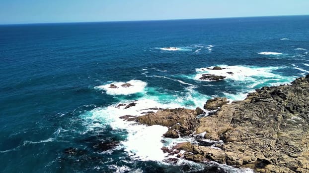 A stunning view of the majestic ocean waves gracefully interacting with the rocky coast under clear blue skies