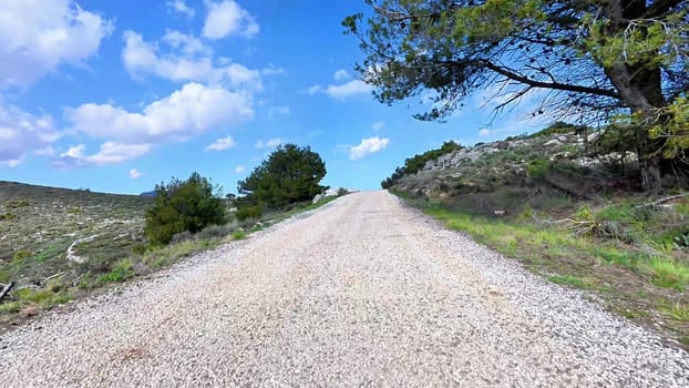 A beautiful, scenic gravel road winds its way through vibrant, lush greenery and rocky terrain beneath a clear blue sky