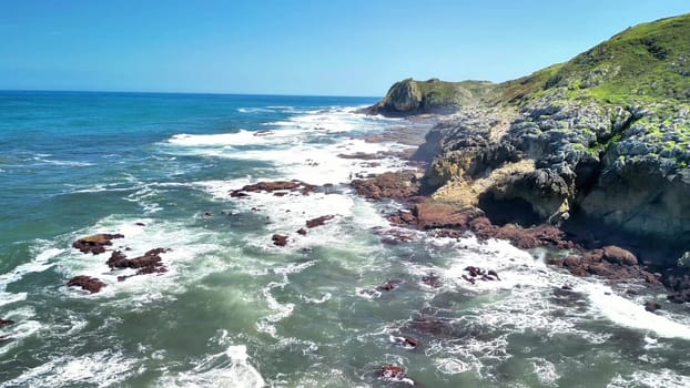 Aerial shots captured from above of waves crashing against a dramatic and rugged rocky coastline under clear blue skies