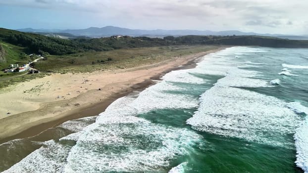 A stunning aerial shot captures the gorgeous beach, gently rolling waves, and lush greenery in the background