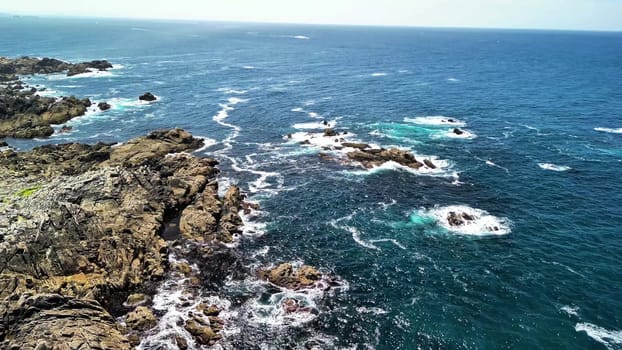 Experience stunning aerial footage of a rocky coastline merging with turquoise sea waves for a picturesque view