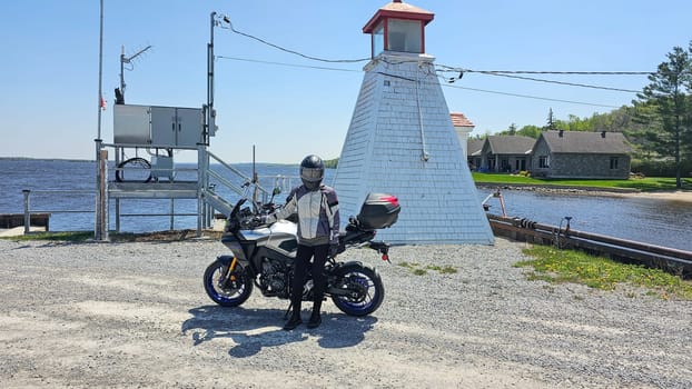 A motorcycle rider pauses at a picturesque lighthouse during a road trip. Perfect for travel enthusiasts and adventure seekers looking for scenic routes and memorable experiences.