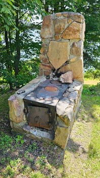 A vintage stone fireplace with an oven, set outdoors among lush greenery. This rustic cooking structure enhances outdoor living spaces, ideal for photos showcasing cooking and craftsmanship.