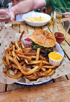 Indulge in a savory burger and crispy fries served on a wooden table in a restaurant. Perfect for casual dining, pub fare, or a tasty meal out. Enjoy the classic combination with dips and drinks.