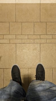 A view of casual black sneakers and faded blue jeans on a neutral earth-toned tile floor. This image captures a relatable everyday moment, ideal for lifestyle themes and backgrounds.