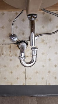 A close-up of plumbing under a bathroom sink shows a P-trap and drain pipe amidst supply lines against a tiled wall, illustrating common plumbing components in home repair.
