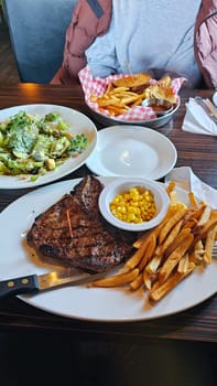Savor a delicious steak dinner with a tender, grilled steak, a fresh garden salad, crispy French fries, and sweet corn. A perfect meal for food lovers and culinary enthusiasts.