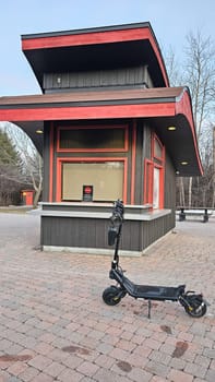 An electric scooter is parked on a brick-paved area near a closed concession stand. This urban scene highlights transportation and recreation in a city outdoor setting.