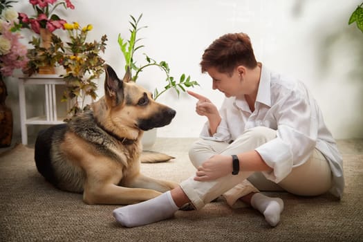 A middle-aged woman interacts with her German Shepherd in a cozy room filled with plants and warm light.
