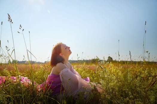 A young woman enjoys the warmth of the sun while sitting peacefully in a vibrant meadow surrounded by blooming flowers.