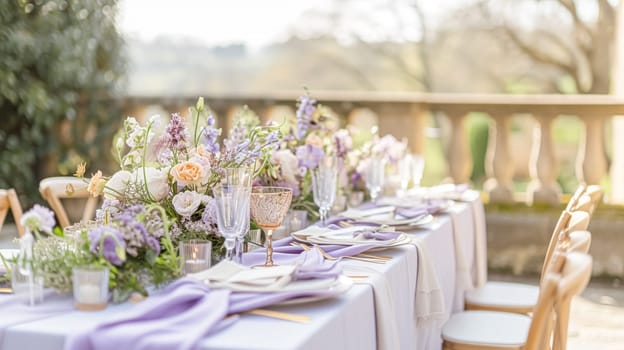 Elegant outdoor dining table set for a celebration in a beautiful garden with a historic building backdrop and purple lavender bushes.