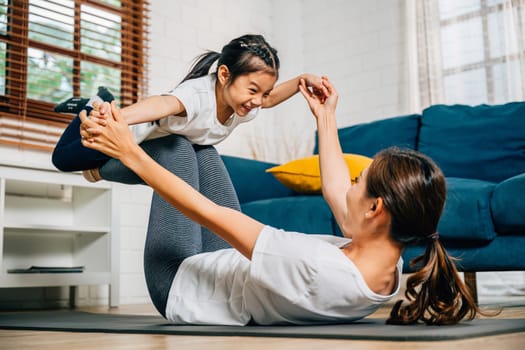 A mother and her daughter enjoy a playful yoga routine at home focusing on the little bird posture. Their smiles reflect a harmonious and joyful family moment filled with trust and balance.