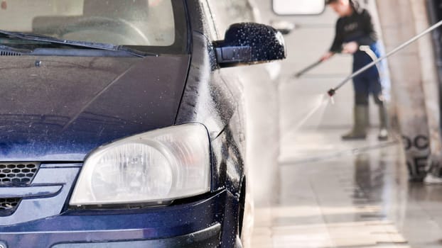 Car wash worker spraying foam and cleaning vehicle with high pressure water jet