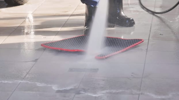 Car wash worker using high pressure water jet to clean car mat