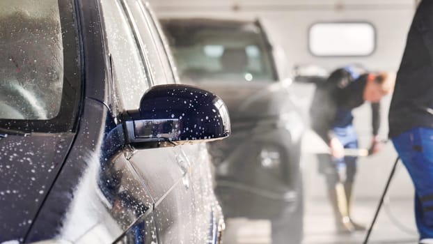Car wash workers cleaning vehicle with high pressure water jet in a professional car wash