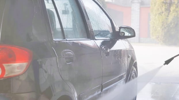 Car wash worker cleaning vehicle with high pressure water jet