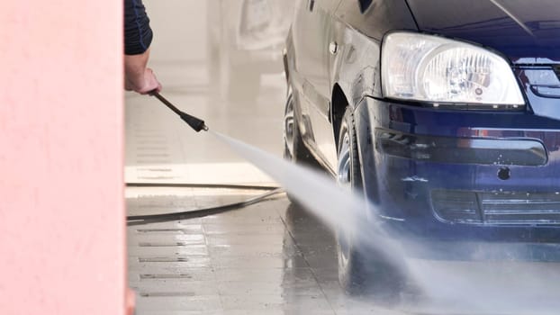 Car wash employee cleaning vehicle with high pressure water jet