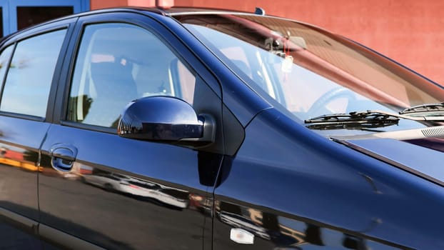 Polished car parked near a building, reflecting the surrounding environment in its paint, shows a concept of car washing and care