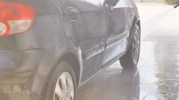 Car wash worker cleaning gray car with high pressure water jet
