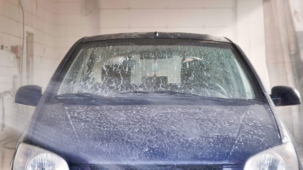 Car is being washed with soap and high pressure water jet in carwash station