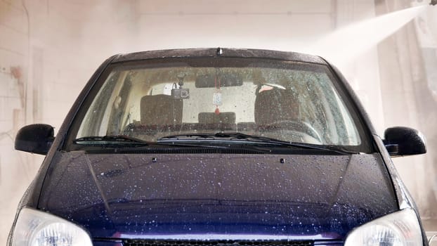 Car wash worker cleaning vehicle with pressurized water in a car wash station